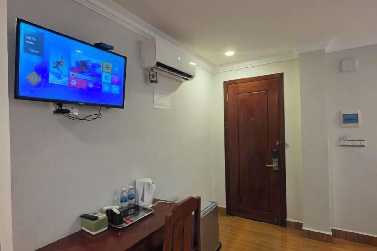 Una camera d'albergo con una TV fissata al muro, una scrivania in legno con un bollitore e una porta che dà su un'altra stanza.