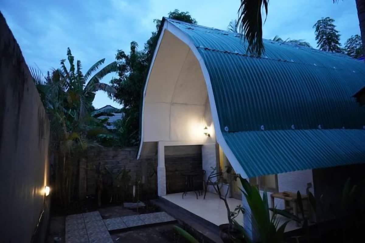 A house with a curved roof, a stone wall, and a small patio area with a table and chairs.