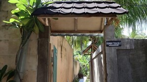 A narrow pathway leading to a covered entrance with a sign reading "Rumah Tiga Gili".