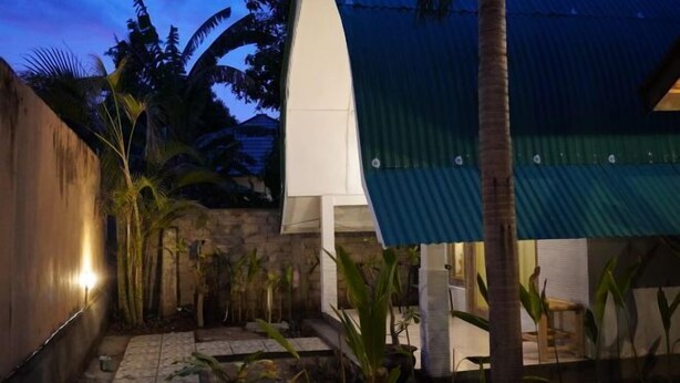 A courtyard with a stone pathway, palm trees, and a covered seating area.