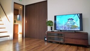 Un salon moderne avec un plancher en bois, une porte coulissante, un téléviseur à écran plat posé sur un meuble en bois et une plante en pot.