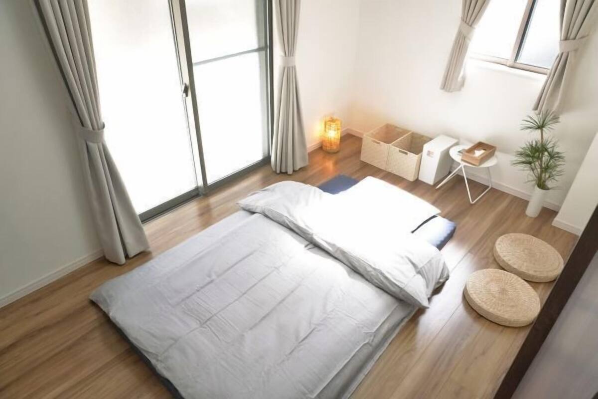 Een slaapkamer met een bed, nachtkastje, lamp en raam met gordijnen.