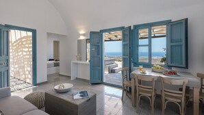 A spacious living area with a view of the sea, a dining area with a table and chairs, and a cozy seating area with a sofa and ottoman. - GTK Santorini Oia Sunset Villas (Santorini)