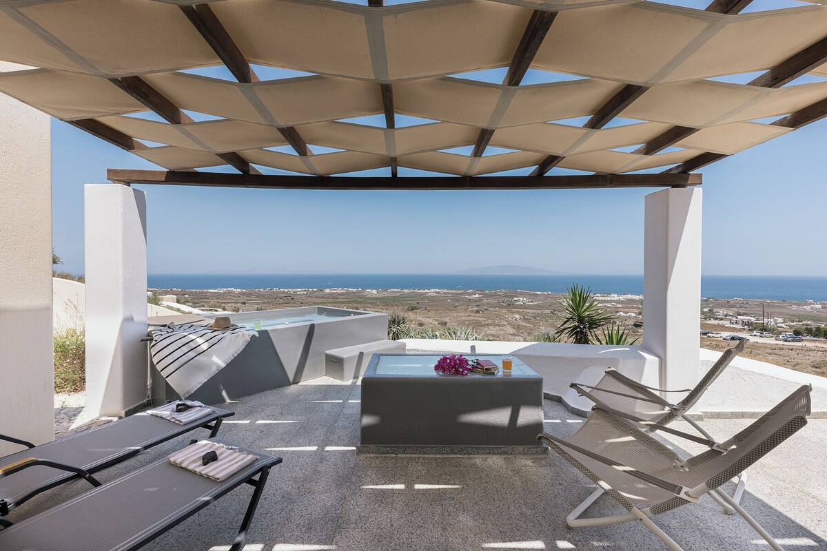 En terrass med utsikt över havet, utrustad med en pergola, solstolar och ett bord.