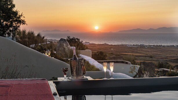 A terrace with a sunset view, a bottle of champagne, and glasses on a table. - GTK Santorini Oia Sunset Villas (Santorini)