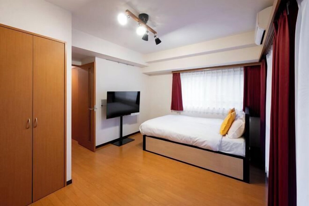 Ein Schlafzimmer mit Bett, Fernseher, Holzschrank und Deckenleuchte.