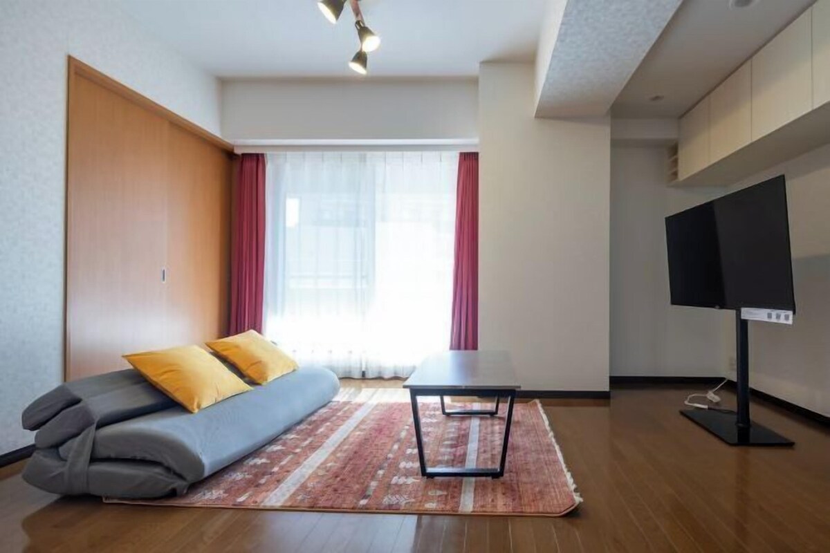 Ein modernes Zimmer mit einer Couch, einem kleinen Tisch, einem Fernseher und einem Fenster mit Vorhängen.