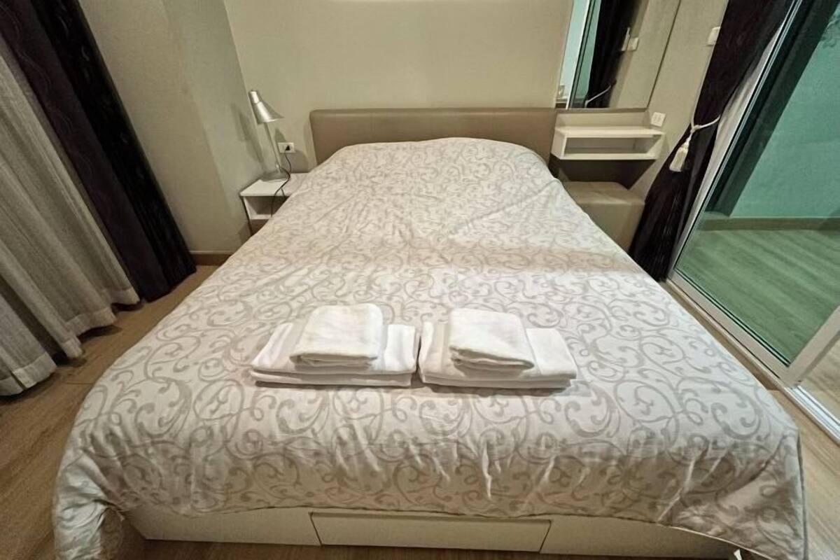 A neatly made bed with a patterned bedspread and two folded towels.