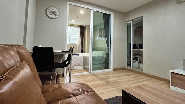 A modern living room with a brown leather sofa, a dining table with chairs, a sliding glass door leading to a bedroom, and a kitchenette area. - Peaceful Stay @MT Khlong Luang (Khlong Luang)