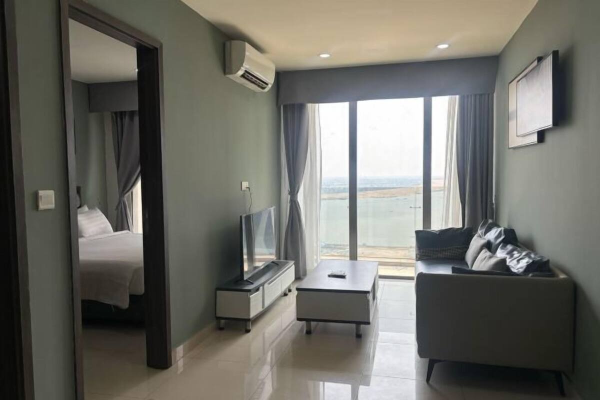 A modern hotel room with a bed, a TV, a sofa, and a large window with a view.