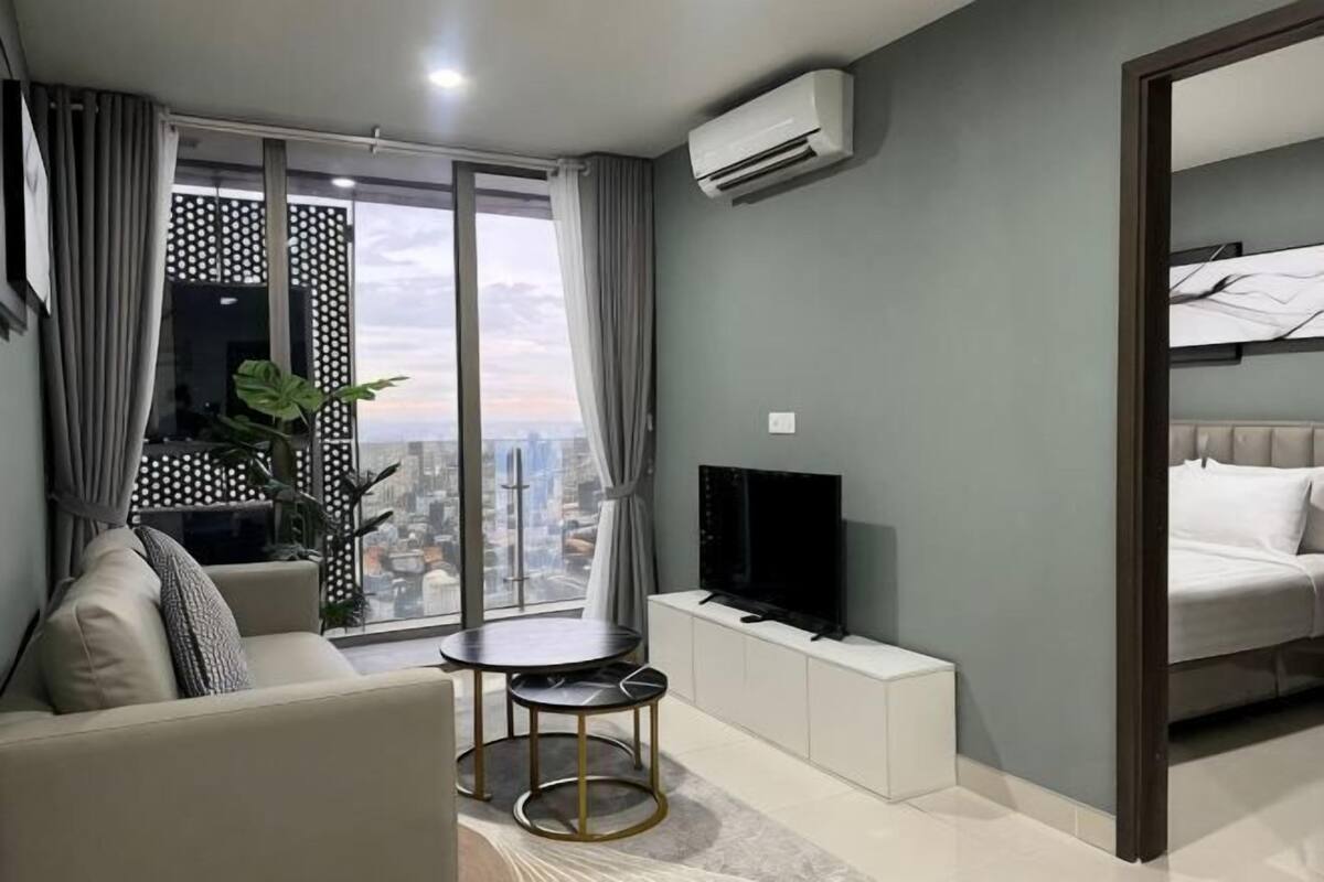 A modern living room with a sofa, a TV, a small table, and a city view through large windows.