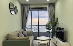 A living room with a sofa, a small round table, a television, and a view of the city through large windows. - The Peak Residence, Multi-Apartment by Emma (Phnom Penh)