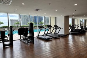 Un gimnasio con equipo de ejercicio, una piscina y grandes ventanales con vistas a la ciudad.
