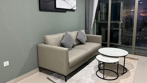 Un salon moderne avec un canapé et deux tables rondes, une grande fenêtre avec des rideaux et des œuvres d’art abstraites accrochées au mur.