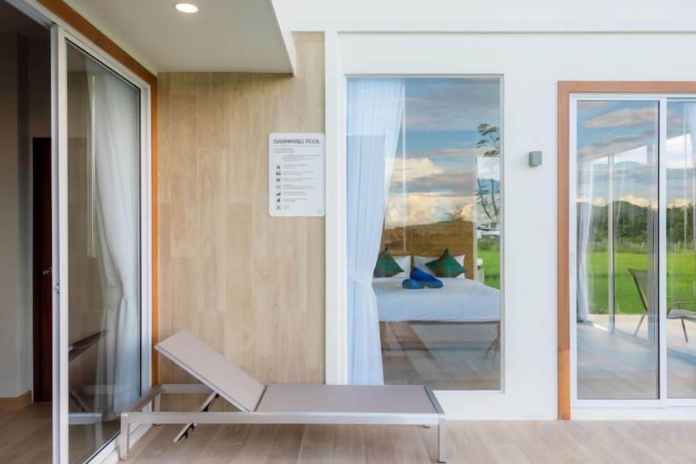 A hotel room with a sliding glass door leading to a balcony, a lounge chair, and a sign indicating a swimming pool.