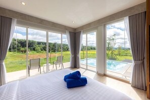 Ein Schlafzimmer mit einem großen Bett, Blick auf einen Pool und eine grüne Landschaft.