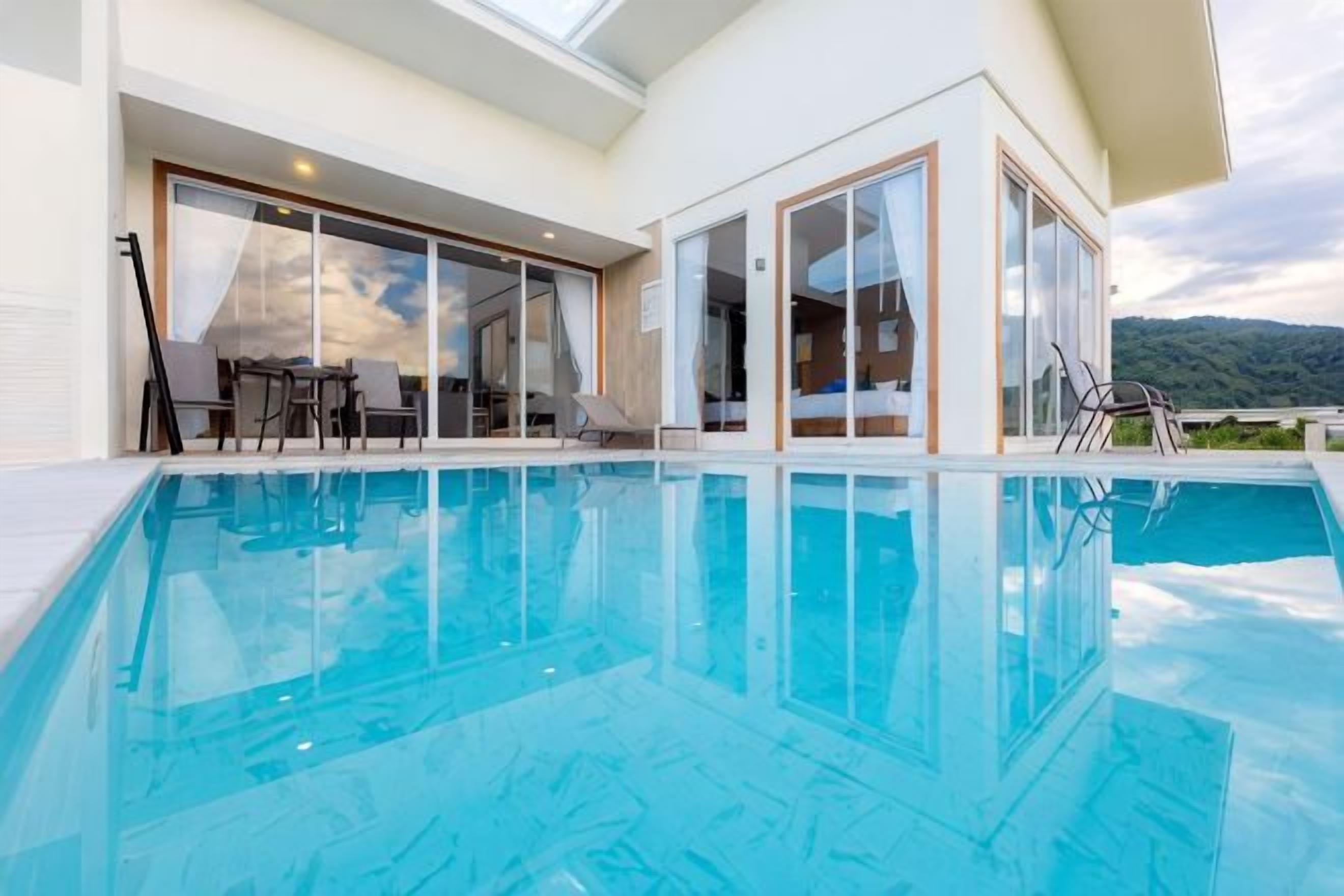 A swimming pool with clear blue water, surrounded by a modern building with large glass doors and windows.