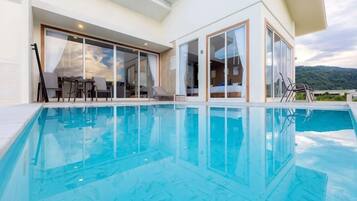 A swimming pool with clear blue water, surrounded by a modern building with large glass doors and windows.