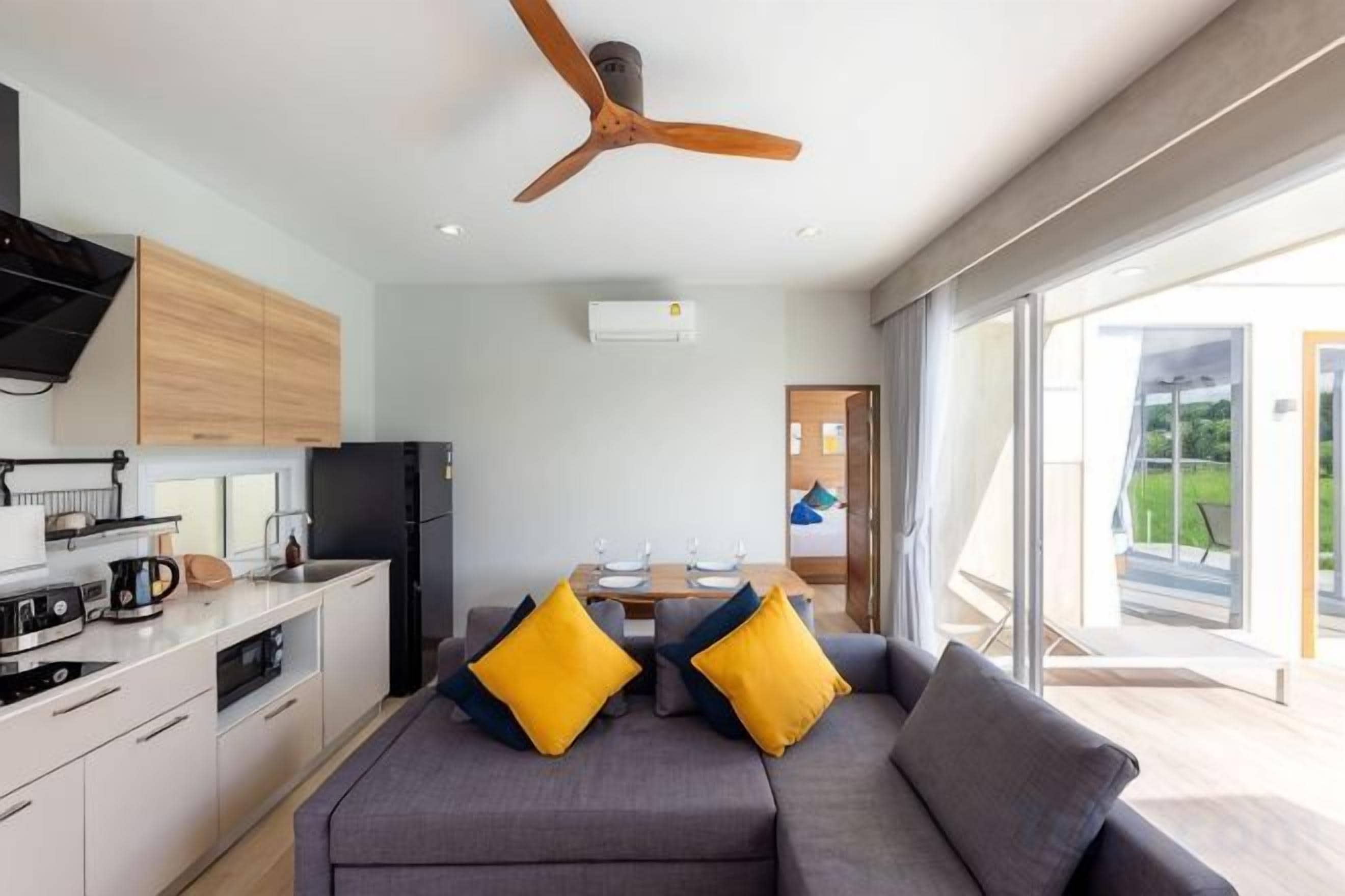 A modern kitchen with a ceiling fan, a dining area with a table and chairs, and a sofa with yellow cushions.