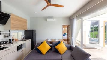 A modern kitchen with a ceiling fan, a dining area with a table and chairs, and a sofa with yellow cushions.