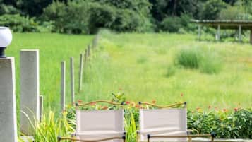A serene outdoor seating area with two chairs and a lamp post, surrounded by lush greenery and a fence.