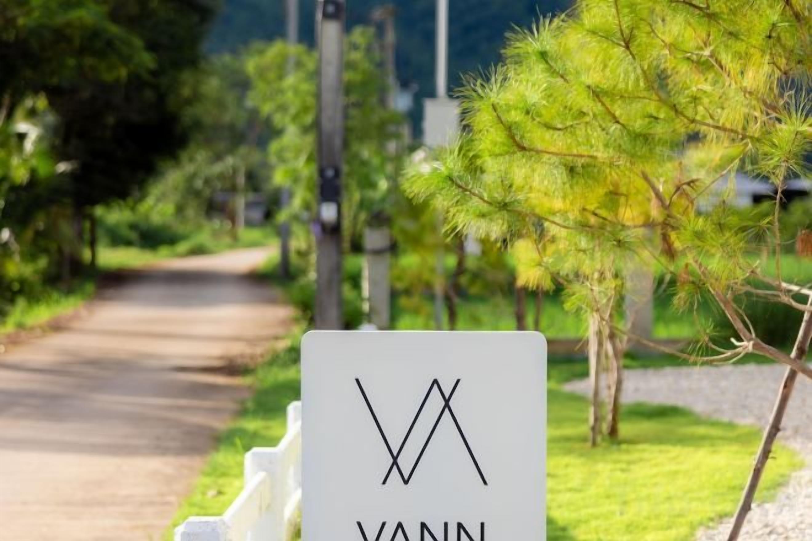 A sign with the name 'YANN' in a rural setting with a dirt path and greenery.