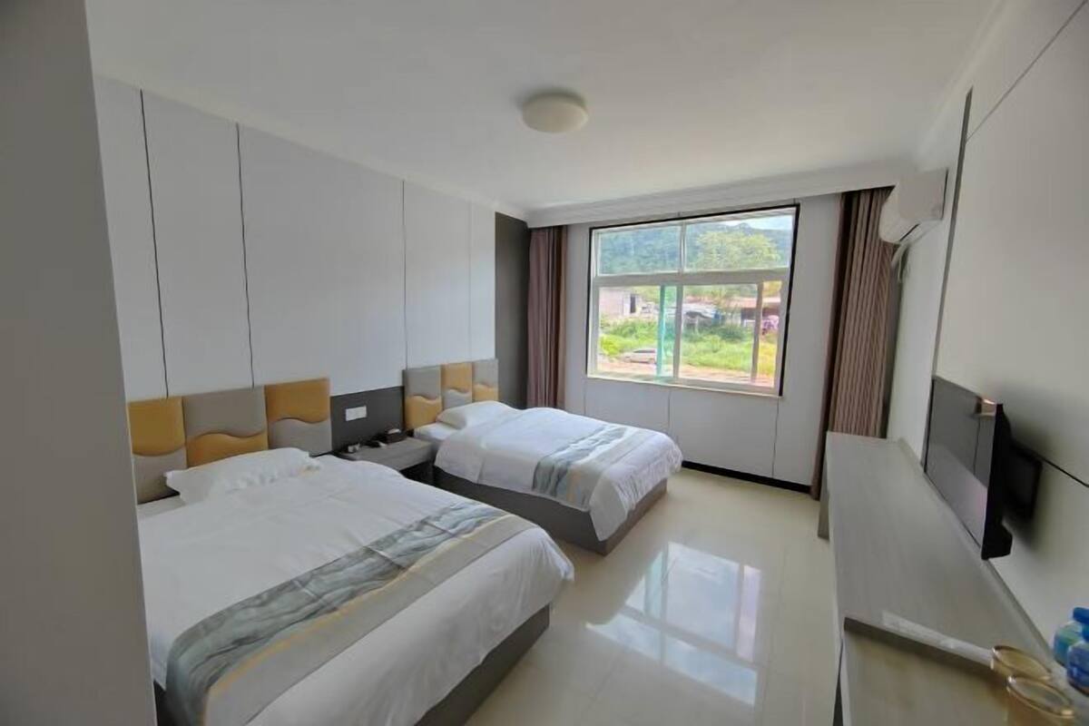 A hotel room with two beds, a flat-screen TV, and a large window with a view of greenery.