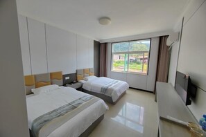 A hotel room with two beds, a flat-screen TV, and a large window with a view of greenery. - Ming Hua International Hotel (Boten)