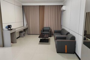 A modern hotel room with a sofa, a small table, a desk, and a curtain. - Ming Hua International Hotel (Boten)