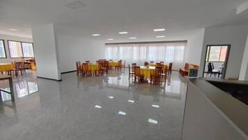 A spacious room with a polished floor, multiple tables with chairs, and large windows allowing natural light.