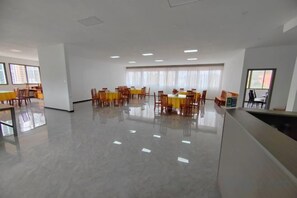 A spacious room with a polished floor, multiple tables with chairs, and large windows allowing natural light. - Ming Hua International Hotel (Boten)