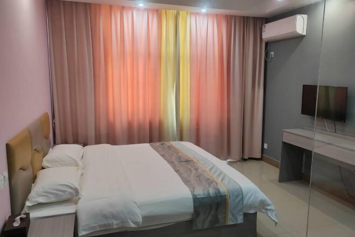 A hotel room with a bed, a desk, an air conditioning unit, and a television.