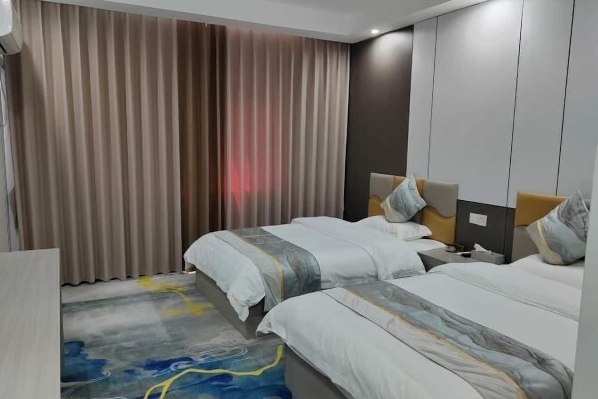 A hotel room with two beds, a large window with curtains, a headboard, and a bedside table.