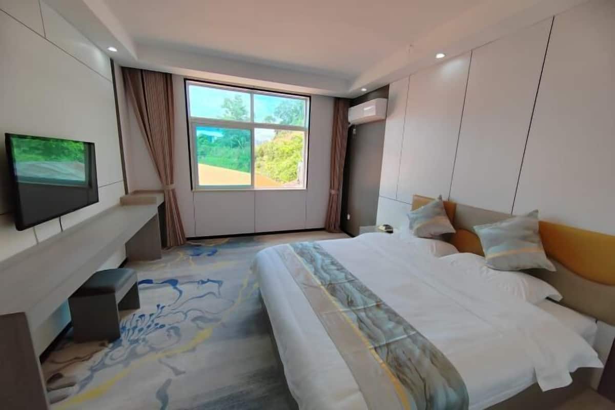 A modern hotel room with a large bed, a flat-screen TV mounted on the wall, and a window with curtains.
