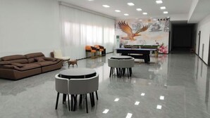 A spacious room with a brown sofa, two round tables, and a ping pong table. - Ming Hua International Hotel (Boten)