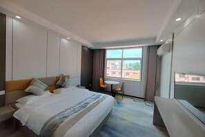 A hotel room with a bed, a small table, a chair, a TV, and a window with a city view. - Ming Hua International Hotel (Boten)