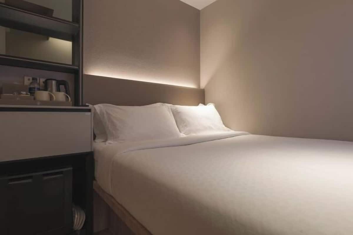 Une chambre d’hôtel avec un lit, une table de chevet et une étagère fixée au mur, sur laquelle sont posés divers objets.