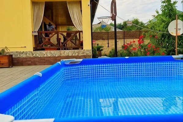 A blue inflatable pool with a tiled floor, surrounded by a wooden deck and a yellow building with a balcony. - Villa Vermont Gusar (Guba)