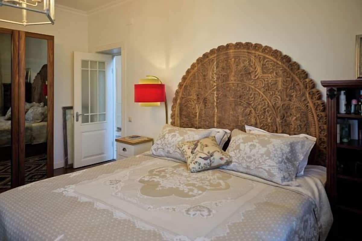 Une chambre à coucher avec un grand lit, une tête de lit en bois, une table de chevet, une lampe rouge et une armoire.
