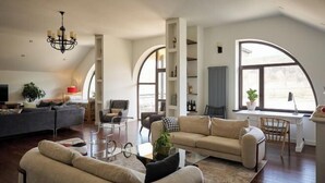 Ein geräumiges Wohnzimmer mit einem großen Bogenfenster, einer Chandelier und einer modernen Sofagarnitur.