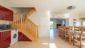 A modern kitchen with red cabinets, a washing machine, a microwave, and a wooden staircase.