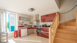 A modern kitchen with red cabinets, a stainless steel range hood, and a wooden staircase.