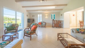 A spacious living area with wicker furniture, large windows, and a view of greenery.