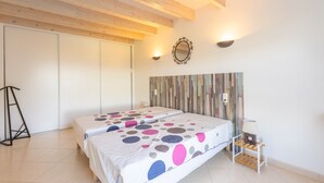 A bedroom with two beds, a wooden ceiling, a wall-mounted mirror, and a bedside table with a lamp.