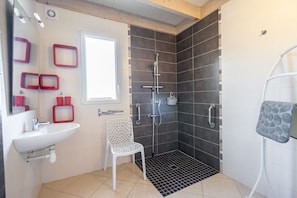 A bathroom with a white sink, a shower with a black floor, and a white chair.