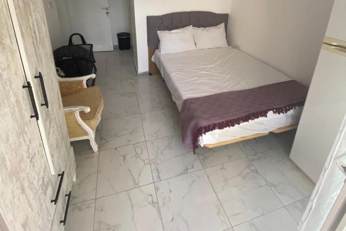 A bedroom with a bed, a wardrobe, a chair, a hanging light, and a door.