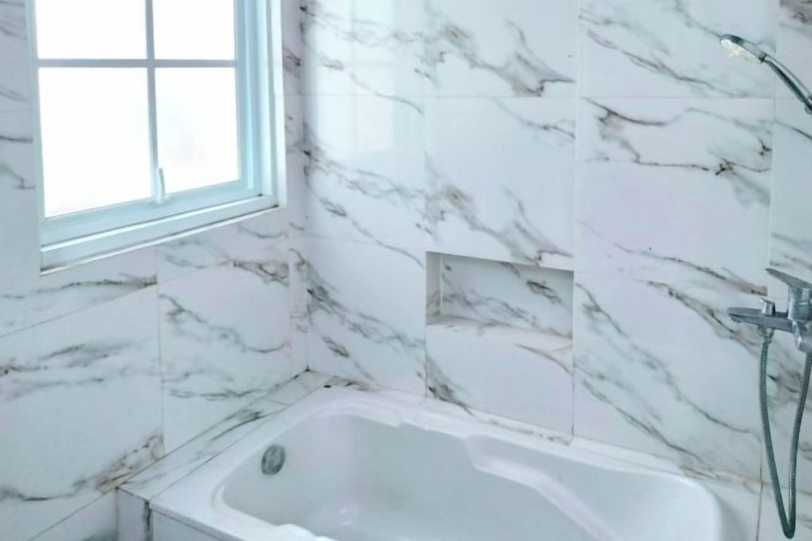 A bathroom with a bathtub, a window, and marble walls.