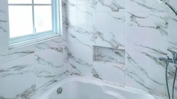 A bathroom with a bathtub, a window, and marble walls.