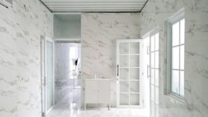 A hallway with marble walls and floor, leading to a room with a large window and a white cabinet. - TwoSpaces Living at Arfina Residence Syariah, Lamongan (Paciran)
