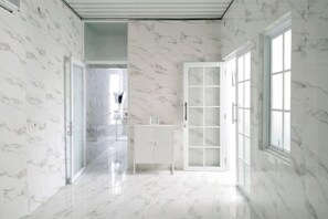 A hallway with marble walls and floor, leading to a room with a large window and a white cabinet. - TwoSpaces Living at Arfina Residence Syariah, Lamongan (Paciran)